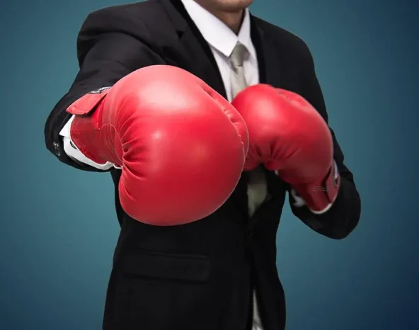 Businessman wearing suit standing professional competition success posture in red boxing gloves isolated on blue background, sport conflict fight knockout concept
