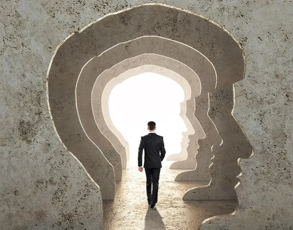 Back view of businessman walking in abstract concrete man head corridor with light. Abstraction and way concept.