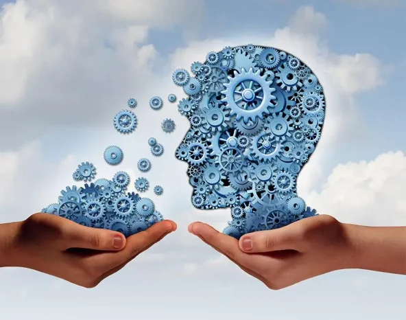 Training and development business education concept with a hand holding a group of gears transferring the wheels to a human head made of cogs as a symbol of acquiring the tools for career learning.